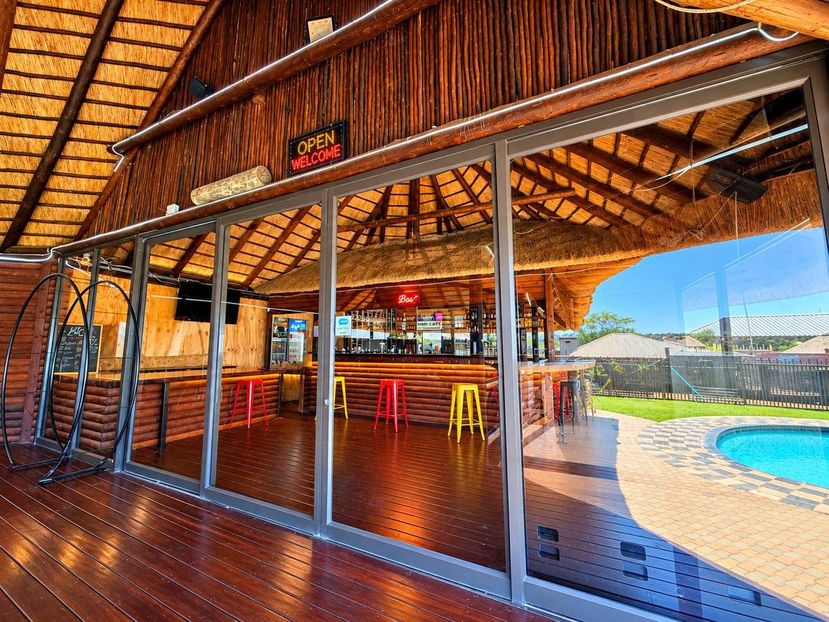 The thatched bar with glass doors opening onto the wooden deck and pool